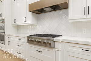 Kitchen with appliances with stainless steel finishes, custom exhaust hood, backsplash, white cabinetry, and light stone counters