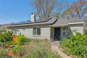 Back of house with brick siding, solar panels, and a chimney