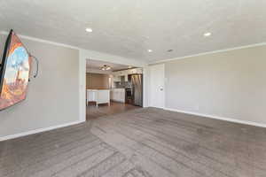 Unfurnished living room with recessed lighting, baseboards, ornamental molding, and dark carpet