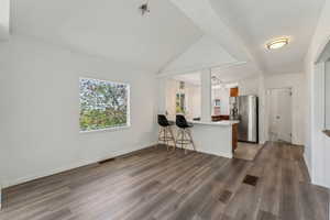 Kitchen with stainless steel refrigerator with ice dispenser, visible vents, wood finished floors, and a peninsula