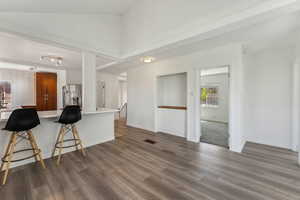 Kitchen with dark wood-style flooring, stainless steel refrigerator with ice dispenser, visible vents, light countertops, and a breakfast bar