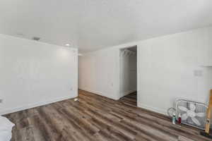 Interior space featuring a textured ceiling, visible vents, baseboards, and wood finished floors