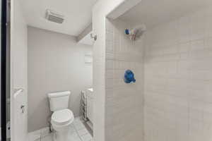Bathroom with tile patterned floors, toilet, tiled shower, and visible vents