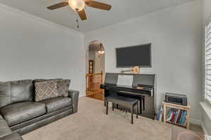 Living area featuring crown molding, ceiling fan, arched walkways, carpet floors, and baseboards