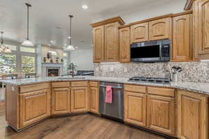 Kitchen featuring appliances with stainless steel finishes, a sink, a peninsula, dark wood-style flooring, and tasteful backsplash