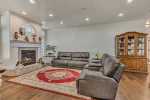 Living room featuring crown molding, a textured ceiling, a fireplace, wood finished floors, and recessed lighting