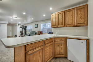 Kitchen with fridge, a peninsula, light countertops, recessed lighting, and brown cabinetry