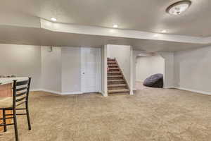 Finished basement featuring a textured ceiling, carpet flooring, baseboards, stairs, and arched walkways