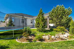 Rear view of house with a trampoline, a yard, and stucco siding