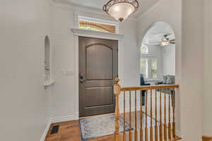 Entrance foyer with arched walkways, crown molding, wood finished floors, a ceiling fan, and baseboards