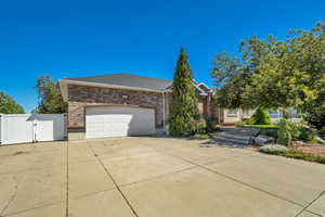 View of front of house with a gate, brick siding, an attached garage, concrete driveway, and roof with shingles