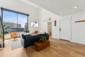 Living room featuring light wood-style floors, a wall mounted AC, recessed lighting, baseboards, and vaulted ceiling
