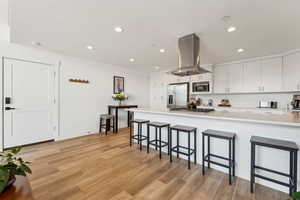 Kitchen with stainless steel appliances, island range hood, a breakfast bar area, light countertops, and light wood finished floors