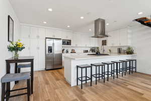 Kitchen with stainless steel appliances, island exhaust hood, a peninsula, a kitchen breakfast bar, and light wood-style floors