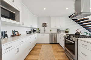 Kitchen with appliances with stainless steel finishes, island range hood, a sink, recessed lighting, and light countertops
