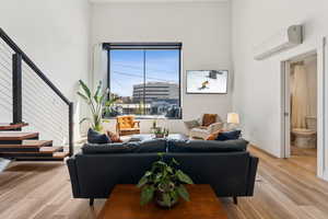 Living room with a wall unit AC, light wood-style floors, stairs, and baseboards