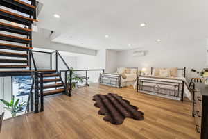 Living area featuring a wall unit AC, wood finished floors, recessed lighting, and stairs