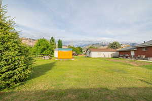 View of grassy yard featuring a storage shed, a patio area, a mountain view, and an outdoor structure
