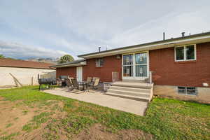 Rear view of property with brick siding, a patio area, a yard, and a mountain view
