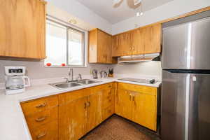 Kitchen featuring freestanding refrigerator, under cabinet range hood, a sink, electric cooktop, and light countertops