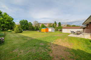 View of green lawn featuring a storage shed, a patio area, an outdoor structure, and a mountain view