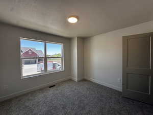 Empty room featuring a textured ceiling, carpet floors, and baseboards