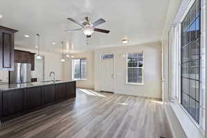 Kitchen featuring freestanding refrigerator, a sink, dark brown cabinets, wood finished floors, and light stone counters