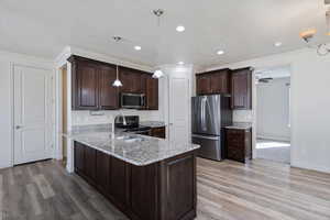 Kitchen featuring appliances with stainless steel finishes, dark brown cabinets, light wood finished floors, crown molding, and a sink