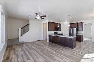 Kitchen with stainless steel appliances, dark brown cabinets, a ceiling fan, a sink, and light wood-type flooring