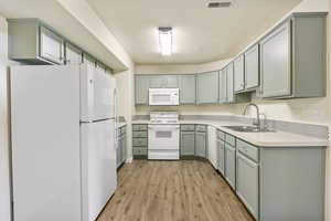 Kitchen with white appliances, a sink, light wood-style flooring, and light countertops