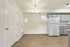 Unfurnished dining area featuring light wood-type flooring, a chandelier, and baseboards