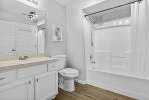 Full bath with wood finished floors, toilet, shower / tub combo with curtain, vanity, and baseboards