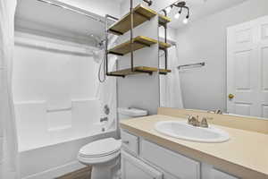 Bathroom featuring toilet, wood finished floors, vanity, and shower / bathtub combination with curtain