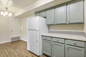 Kitchen with freestanding refrigerator, light countertops, light wood-style floors, baseboards, and a chandelier
