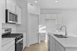 Kitchen with stainless steel appliances, light wood-style flooring, a sink, white cabinetry, and recessed lighting