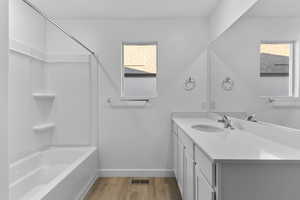 Full bath with baseboards, wood finished floors, vanity, and shower / bath combination