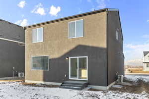 Snow covered house featuring ac unit and stucco siding