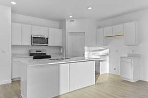 Kitchen featuring stainless steel appliances, a sink, white cabinets, a kitchen island with sink, and light wood finished floors