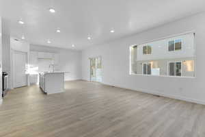 Unfurnished living room with recessed lighting, light wood-style flooring, baseboards, and a sink
