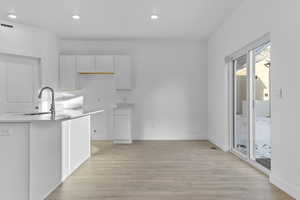 Kitchen with a sink, white cabinetry, light wood-style floors, recessed lighting, and baseboards