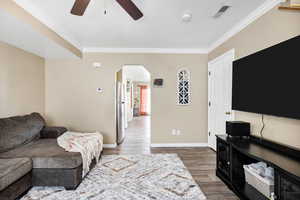 Living room featuring arched walkways, ornamental molding, a ceiling fan