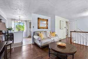 Living area with a textured ceiling, a chandelier, hardwood / wood-style floors, and baseboards