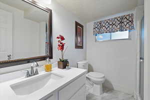 Bathroom featuring marble finish floors, toilet, shower, a textured ceiling, and vanity