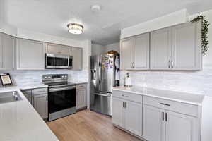 Kitchen featuring appliances with stainless steel finishes, gray cabinetry, light wood-type flooring, a textured ceiling, and tasteful backsplash