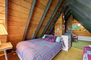 Carpeted bedroom with wood walls and vaulted ceiling