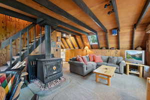 Living room featuring wood walls, a wood stove, carpet floors, and beam ceiling