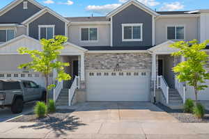 View of front facade featuring driveway, stone siding, and a garage