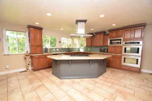 Kitchen featuring appliances with stainless steel finishes, island range hood, brown cabinets, and recessed lighting