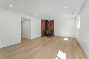 Unfurnished living room featuring a wood stove, light wood finished floors, baseboards, and recessed lighting