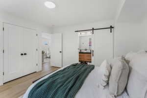 Bedroom with light wood finished floors, a barn door, and ensuite bathroom